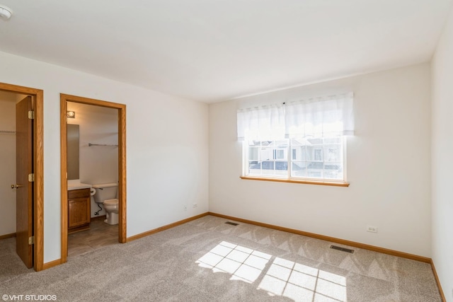 unfurnished bedroom with light carpet, visible vents, a walk in closet, and baseboards