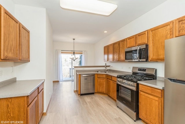 kitchen featuring light wood-type flooring, a peninsula, brown cabinetry, stainless steel appliances, and a sink