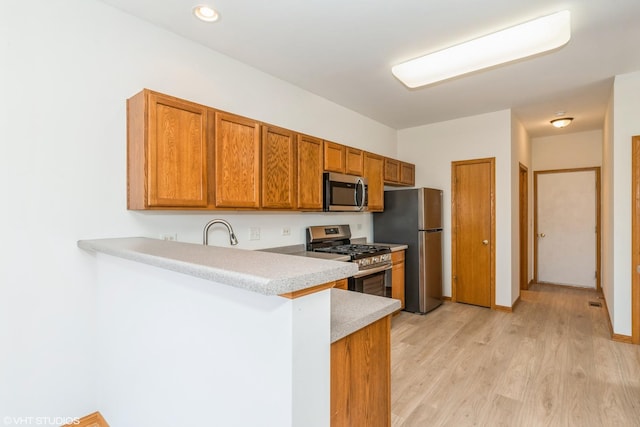 kitchen featuring light countertops, light wood-style flooring, brown cabinets, a peninsula, and stainless steel appliances