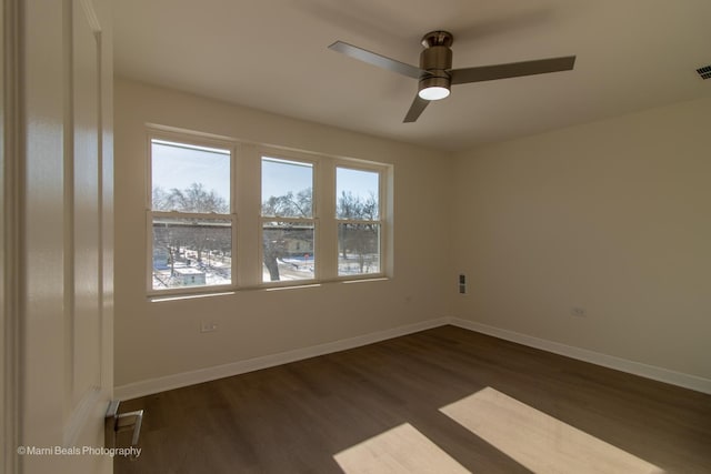 spare room featuring visible vents, baseboards, ceiling fan, and dark wood-type flooring