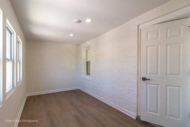 unfurnished room with brick wall, dark wood-style flooring, recessed lighting, and baseboards