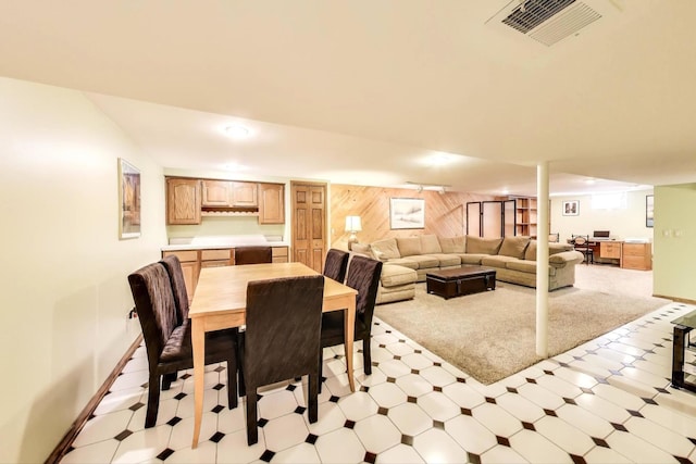 dining room featuring light floors, visible vents, wood walls, and baseboards