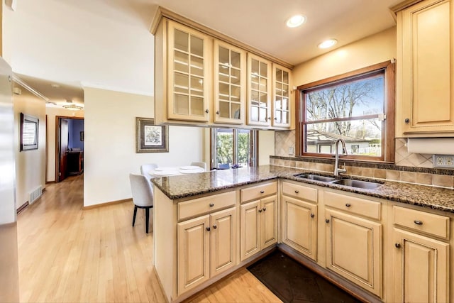 kitchen featuring baseboards, a peninsula, a sink, decorative backsplash, and light wood-type flooring