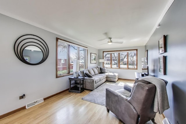 living room with baseboards, visible vents, light wood finished floors, ceiling fan, and ornamental molding