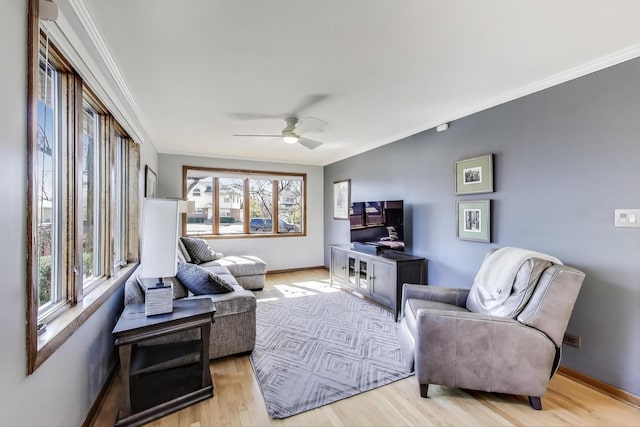 living area with baseboards, a ceiling fan, light wood-type flooring, and ornamental molding