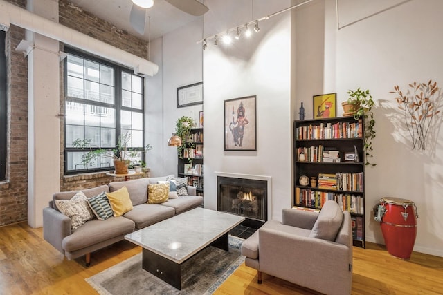 living area with light wood-type flooring, ceiling fan, brick wall, and a high ceiling