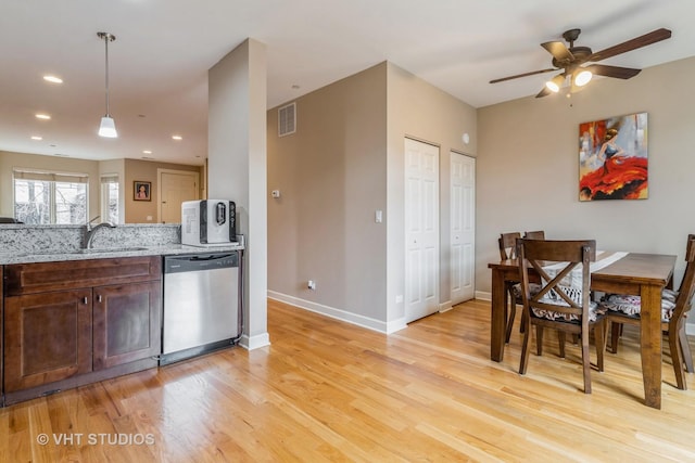 kitchen with a sink, visible vents, light wood-style floors, light stone countertops, and dishwasher