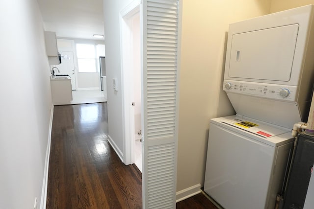 laundry area with stacked washer / dryer, dark wood-type flooring, and sink