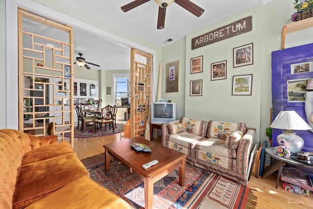 living room with ceiling fan, visible vents, and wood finished floors