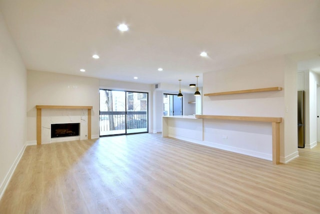 unfurnished living room featuring light wood-style floors, recessed lighting, baseboards, and a high end fireplace