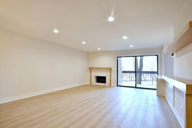 unfurnished living room with a high end fireplace, baseboards, light wood finished floors, and recessed lighting