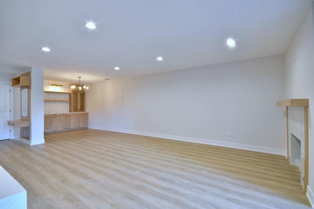 unfurnished living room with light wood-style flooring, a fireplace, a chandelier, and recessed lighting