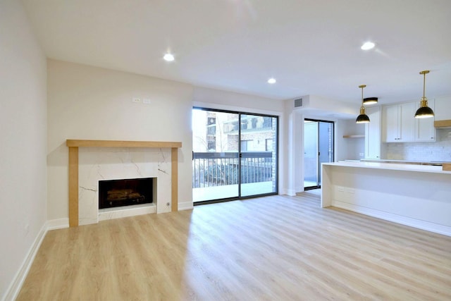 unfurnished living room with light wood-style floors, a high end fireplace, and recessed lighting