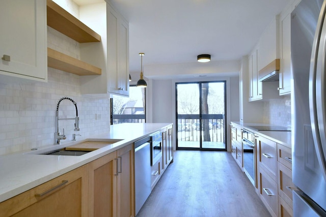 kitchen with appliances with stainless steel finishes, light countertops, light wood-type flooring, open shelves, and a sink