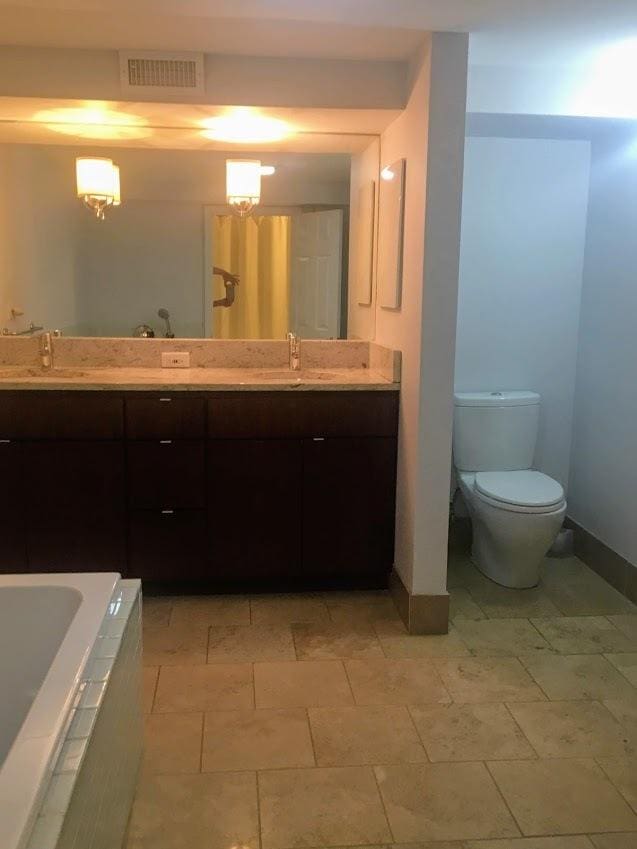 bathroom with visible vents, double vanity, tiled tub, a sink, and toilet