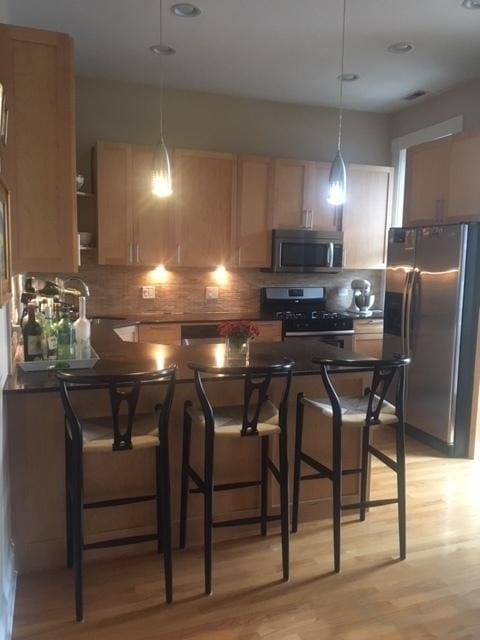 kitchen featuring dark countertops, backsplash, light wood-type flooring, and appliances with stainless steel finishes