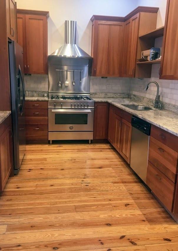 kitchen featuring light wood-style flooring, a sink, open shelves, stainless steel appliances, and wall chimney range hood