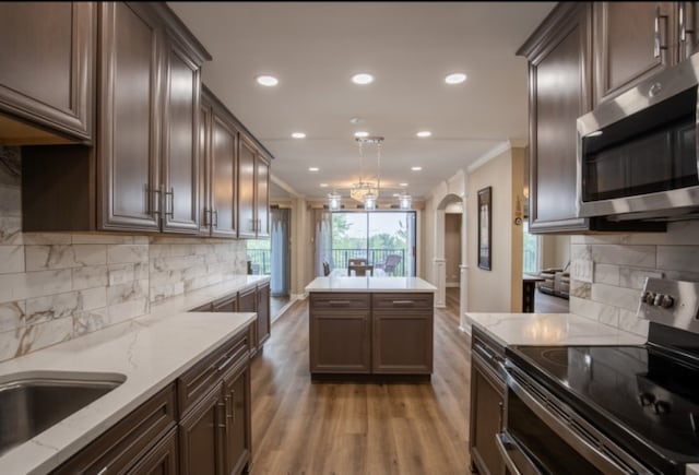 kitchen featuring arched walkways, stainless steel appliances, light wood-style floors, ornamental molding, and decorative light fixtures