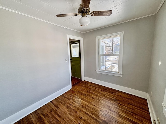 empty room featuring ornamental molding, dark wood-style flooring, a ceiling fan, and baseboards