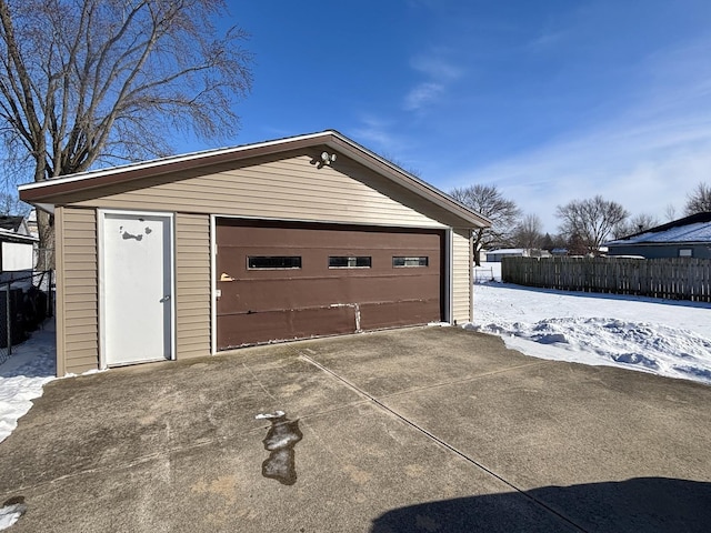 snow covered garage featuring a garage and fence