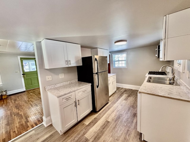 kitchen featuring freestanding refrigerator, light countertops, a sink, and white cabinetry