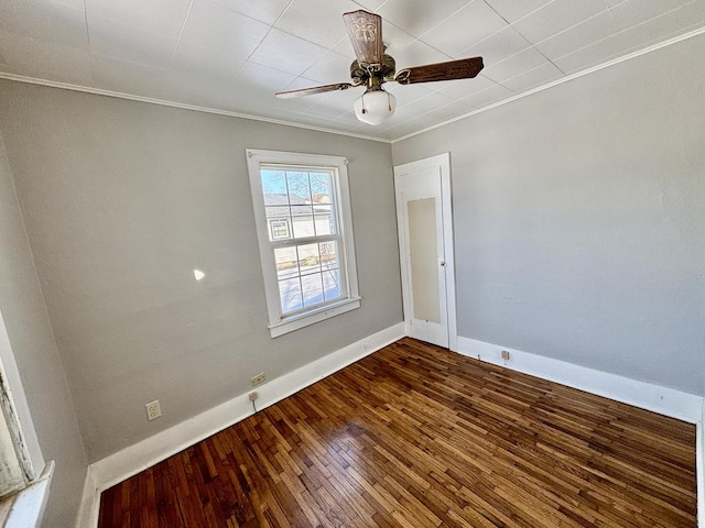 spare room featuring a ceiling fan, dark wood finished floors, crown molding, and baseboards