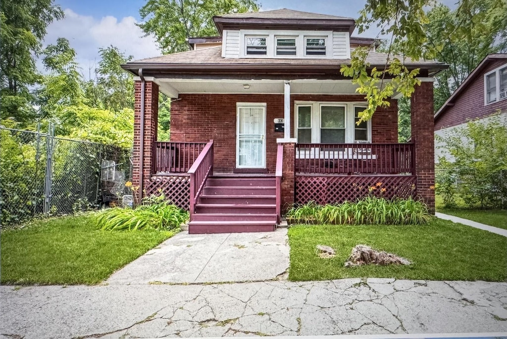 bungalow-style home with covered porch, a front yard, fence, and brick siding