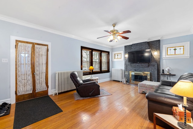 living room featuring light wood-type flooring, ornamental molding, a brick fireplace, and radiator heating unit