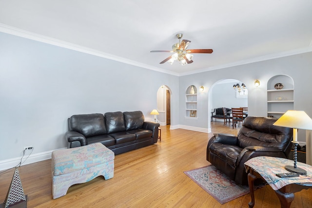 living room with ceiling fan, light hardwood / wood-style flooring, crown molding, and built in shelves