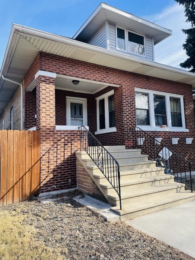 view of front of home featuring covered porch, brick siding, fence, and stairs