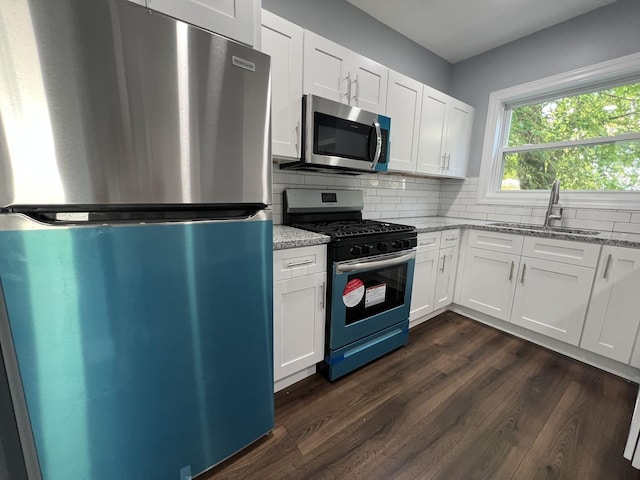 kitchen featuring decorative backsplash, white cabinets, appliances with stainless steel finishes, light stone countertops, and a sink