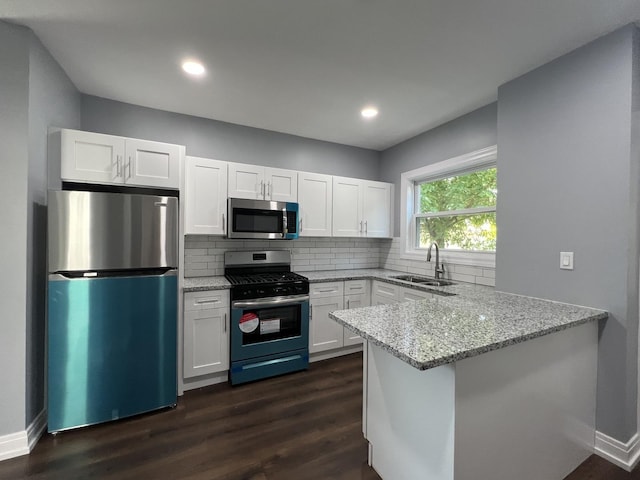 kitchen featuring light stone counters, stainless steel appliances, a peninsula, a sink, and white cabinets