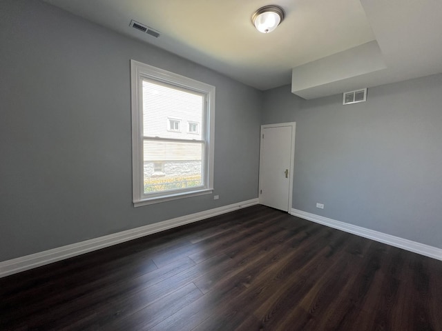 spare room with dark wood-style floors, visible vents, and baseboards