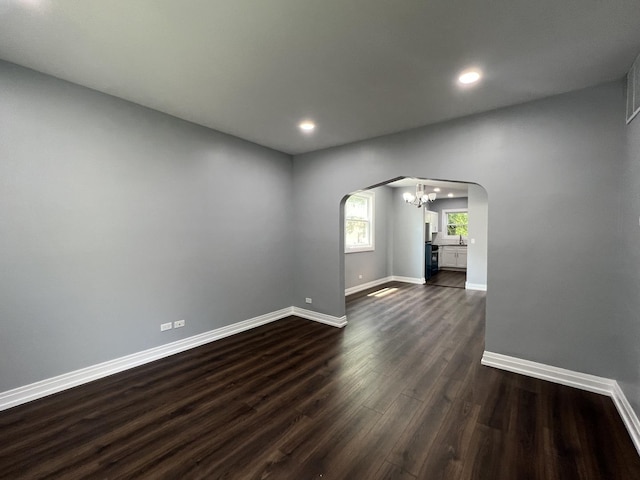 spare room featuring arched walkways, dark wood-style flooring, a notable chandelier, recessed lighting, and baseboards