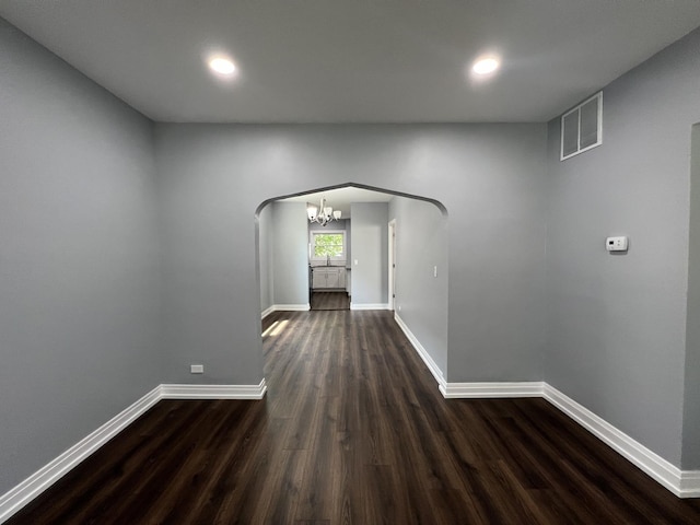 corridor featuring arched walkways, dark wood-style floors, visible vents, and baseboards