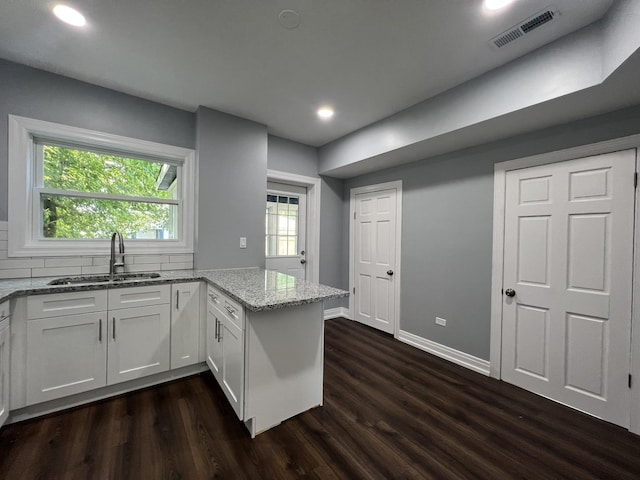 kitchen with light stone counters, dark wood finished floors, visible vents, white cabinets, and a sink