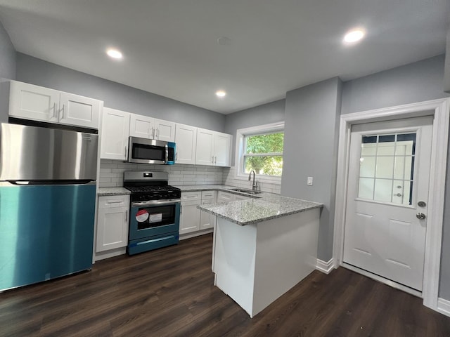 kitchen featuring light stone counters, white cabinetry, stainless steel appliances, and a sink