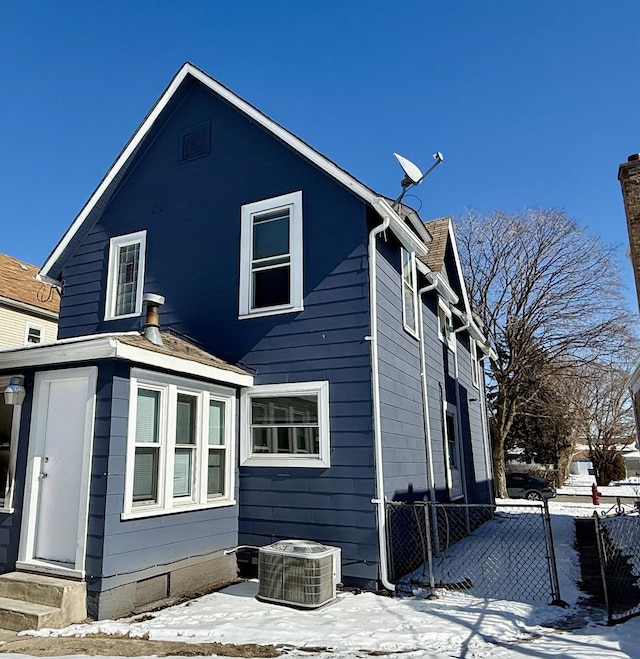 snow covered back of property featuring entry steps, fence, and central air condition unit