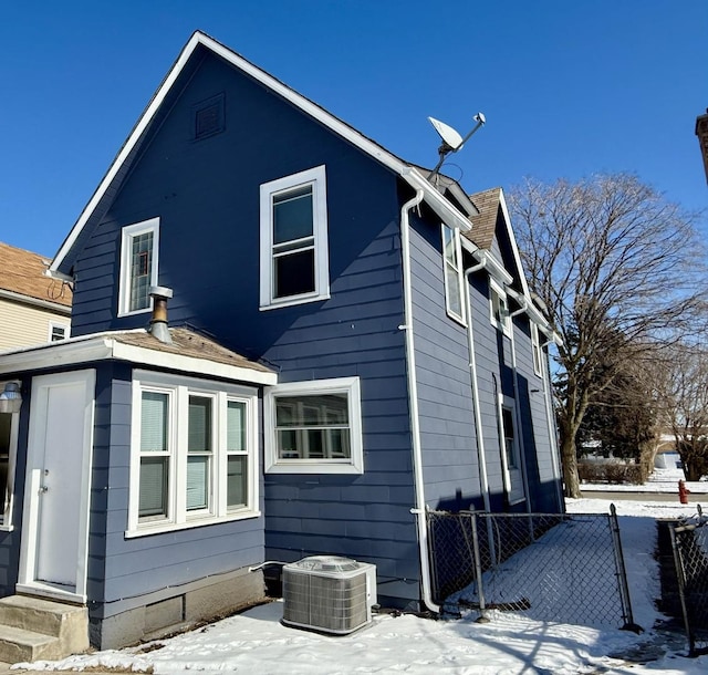 snow covered property with entry steps, central AC, and fence