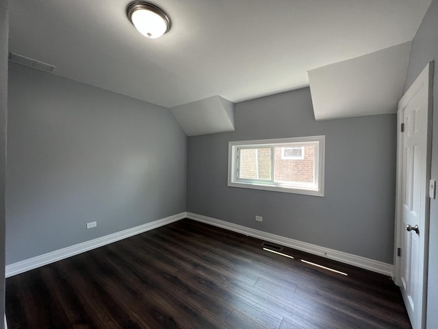 additional living space with dark wood-style floors, lofted ceiling, visible vents, and baseboards