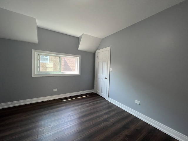 spare room featuring lofted ceiling, visible vents, baseboards, and dark wood finished floors