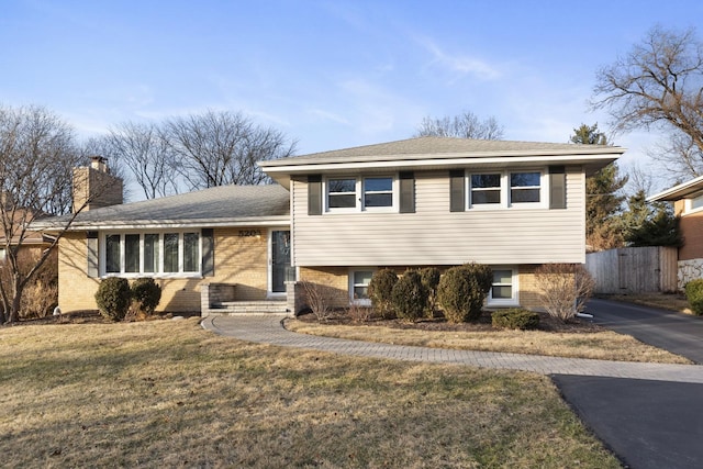 split level home with aphalt driveway, a chimney, brick siding, and a front lawn