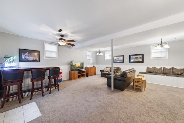 carpeted living room with a bar, ceiling fan with notable chandelier, visible vents, and wainscoting