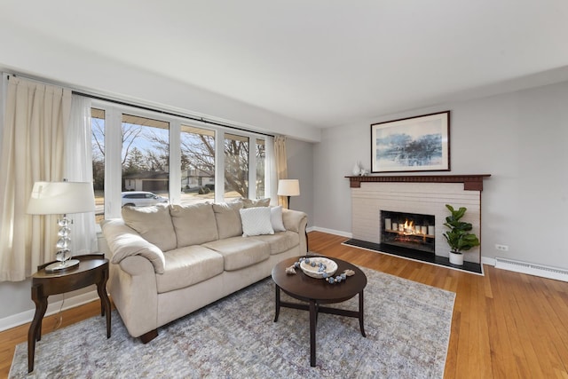 living room featuring wood finished floors, baseboards, a fireplace, and a baseboard radiator