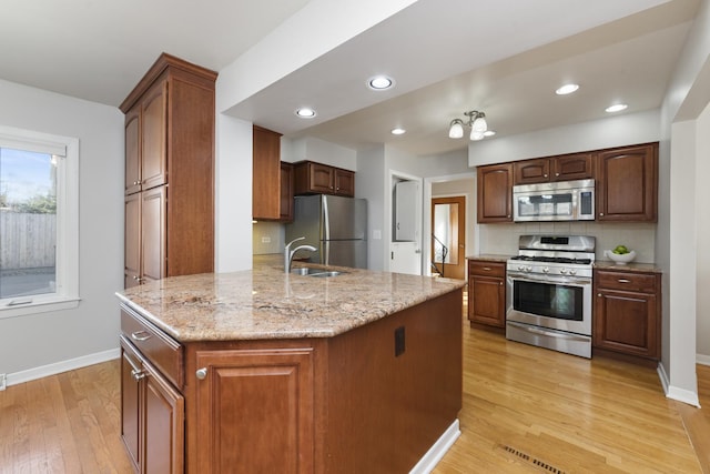 kitchen with light stone countertops, light wood-type flooring, appliances with stainless steel finishes, a peninsula, and a sink