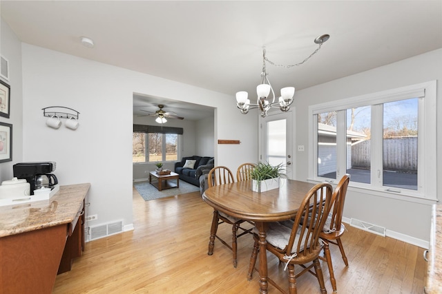 dining space with ceiling fan with notable chandelier, baseboards, visible vents, and light wood-style floors