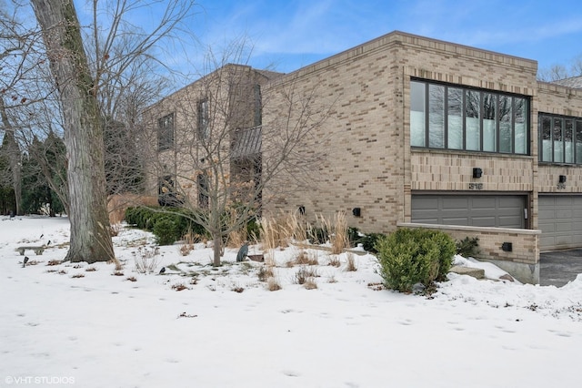 view of snow covered exterior with brick siding and an attached garage