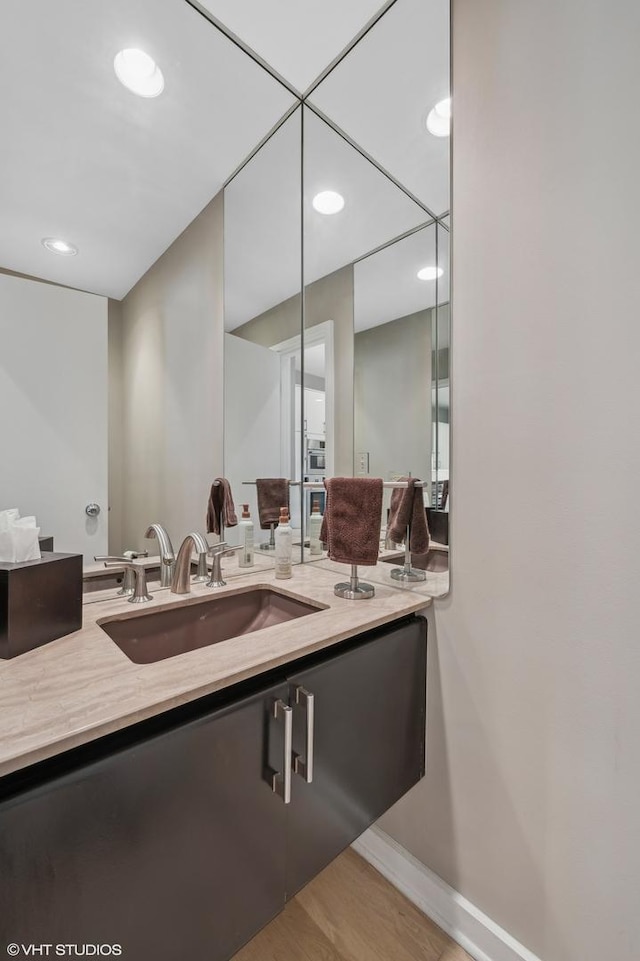 bathroom with recessed lighting, baseboards, wood finished floors, and vanity