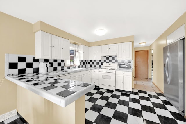 kitchen featuring stainless steel fridge, kitchen peninsula, tile countertops, white gas range, and white cabinetry