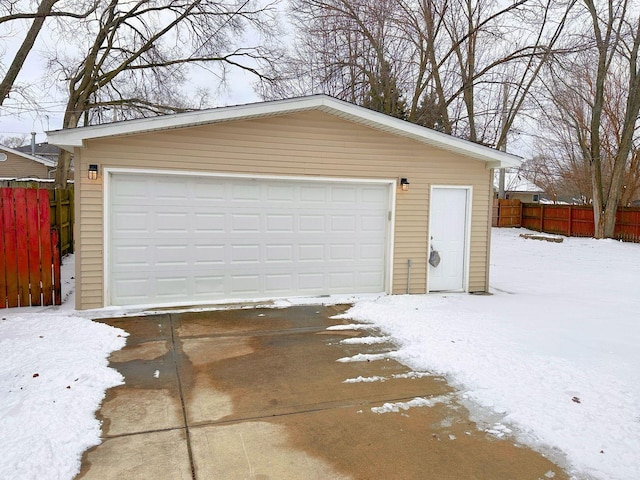 snow covered garage featuring a garage and fence